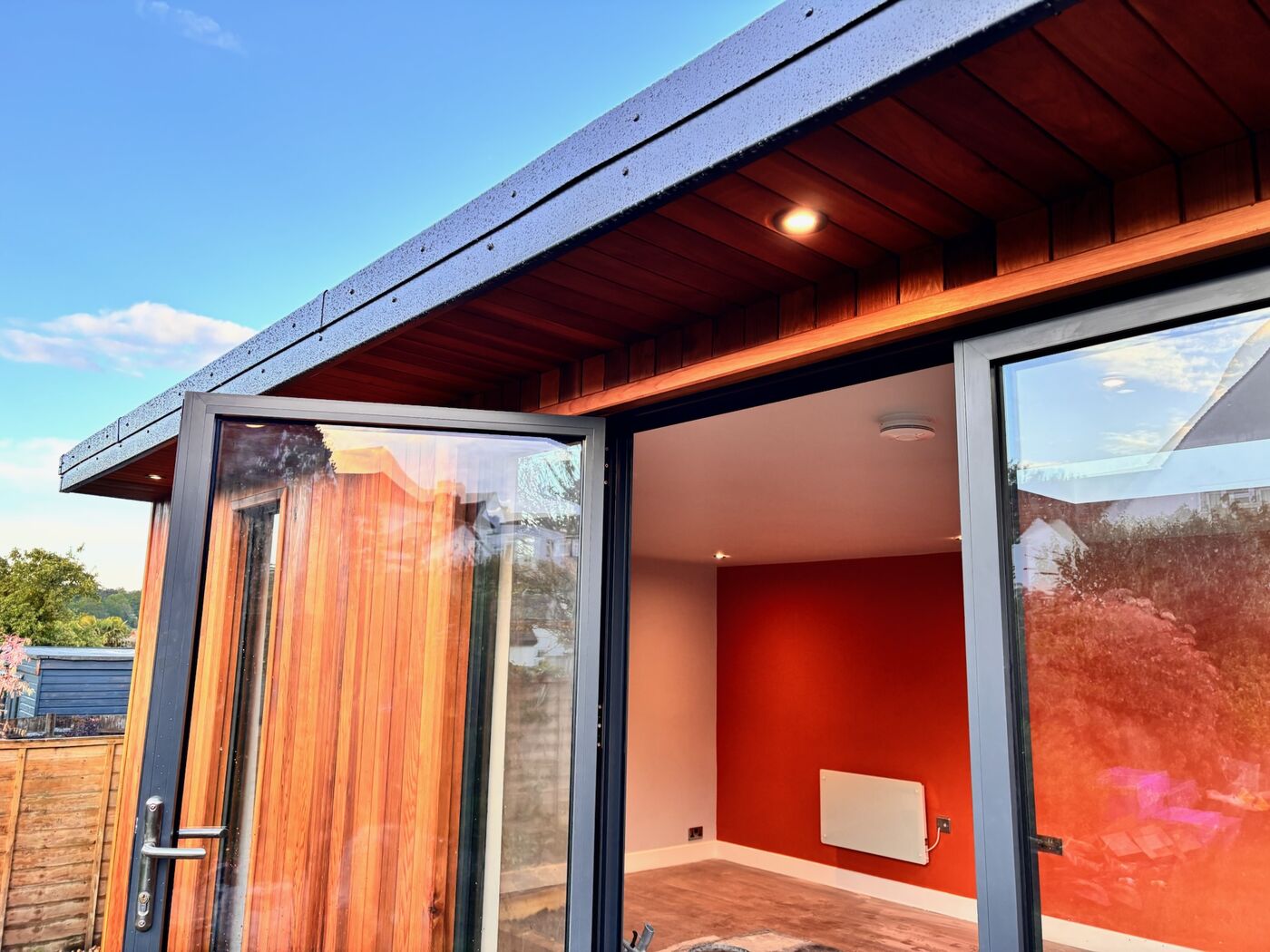 Open glazed doors of a cedar garden room revealing a red feature wall inside