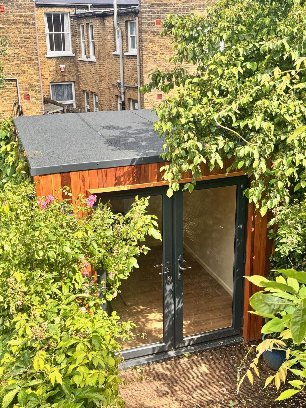 Cedar garden office with grey double doors, seen from above among lush garden planting